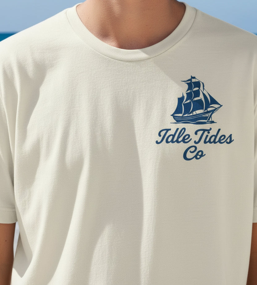 Idle Tides Co ‘Drop Anchor, Stay Awhile’ crewneck tee in vintage white with nautical text graphic across chest, relaxed fit, and dockside lifestyle design.